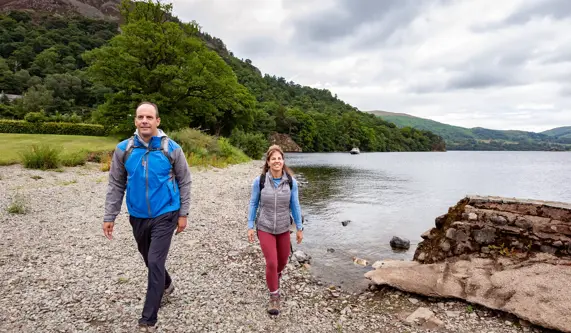 A couple walk along a lakeside pebble beach in England